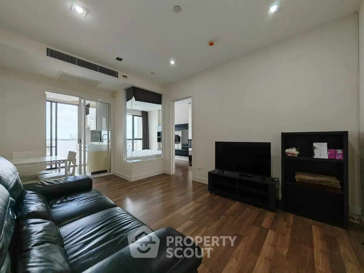 Spacious modern living room with leather sofa and wooden flooring, featuring a view into a bright bedroom.