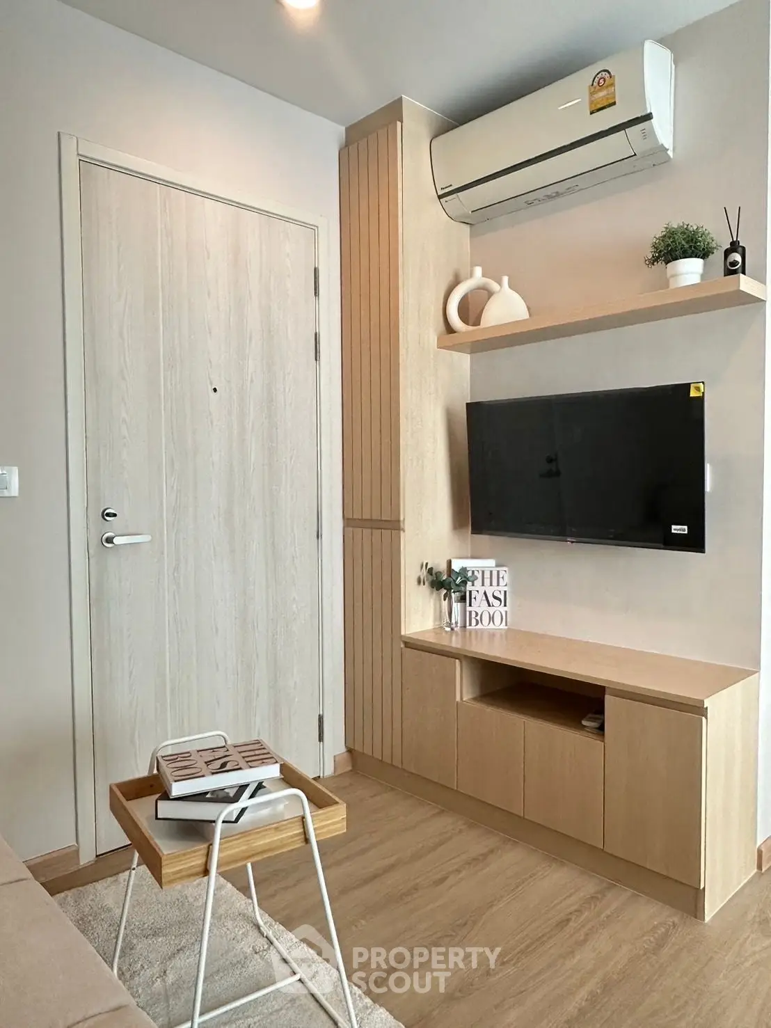 Modern living room with sleek wooden furniture and wall-mounted TV, featuring minimalist decor and air conditioning.