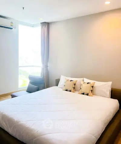 Spacious bedroom with large window and modern decor in a high-rise apartment.