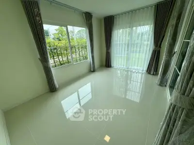 Bright empty room with large windows and elegant curtains, offering a serene garden view.