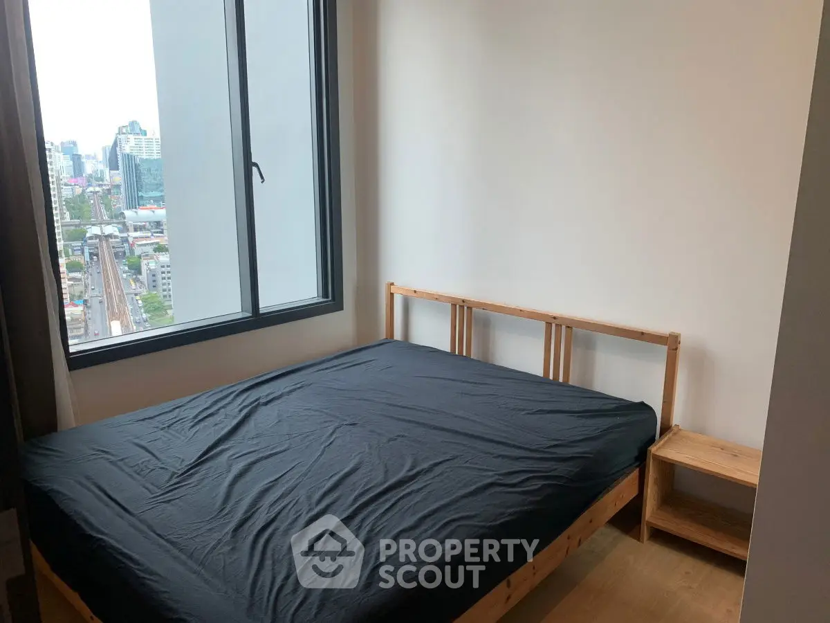 Cozy bedroom with city view, featuring a wooden bed frame and side table, perfect for urban living.