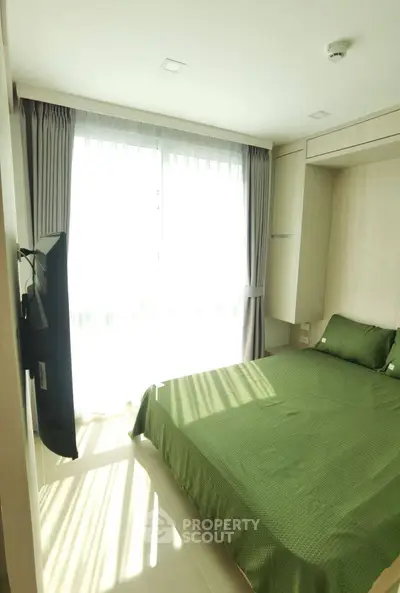 Bright and cozy bedroom with green bedding and large window for natural light.