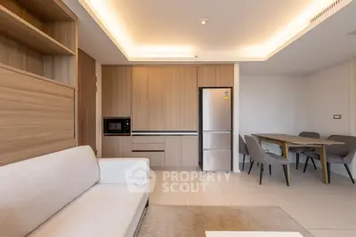 Modern living room with open kitchen and dining area, featuring sleek wooden cabinetry and contemporary furniture.
