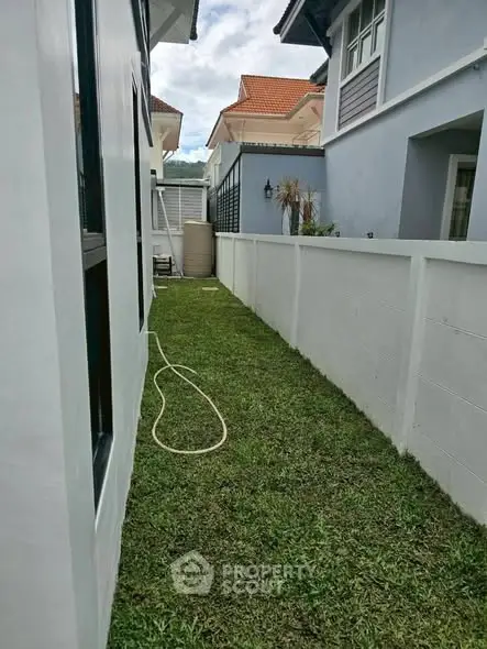 Charming side garden with lush grass between modern homes, perfect for outdoor relaxation.