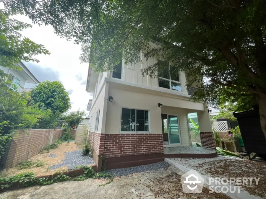 Charming two-story home with a spacious balcony and lush green surroundings, featuring a modern design with brick accents and ample outdoor space for relaxation.