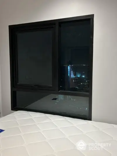 Modern bedroom with large window offering stunning city night view.