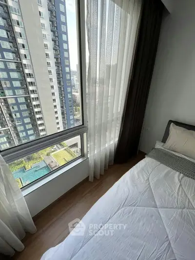 Modern bedroom with large window offering stunning city view in high-rise apartment.