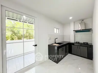 Modern kitchen with sleek black cabinetry and gas stove, adjacent to a bright balcony.