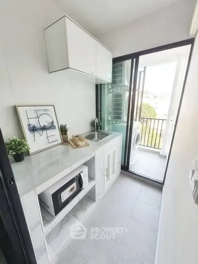 Modern kitchen with sleek design and balcony view, featuring microwave and stylish decor.