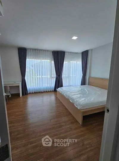 Spacious bedroom with large windows and elegant curtains, featuring a modern bed and wooden flooring.