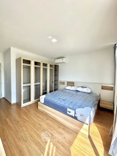 Spacious bedroom with modern wooden flooring and ample natural light, featuring a large bed and built-in wardrobe.