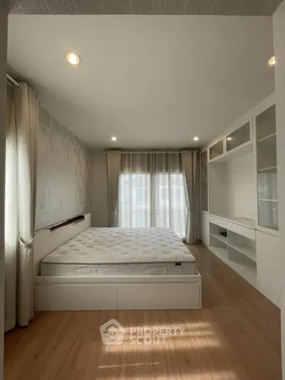 Spacious bedroom with large windows allowing natural light, featuring a comfortable bed and built-in white shelving for ample storage.