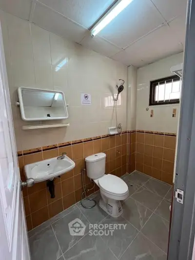 Modern bathroom with tiled walls, compact sink, and toilet in a well-lit space.