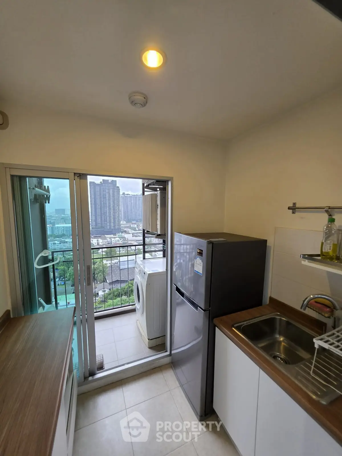 Compact kitchen with balcony view, featuring fridge and washing machine, ideal for urban living.