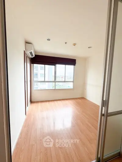 Spacious empty room with wooden flooring and large windows offering natural light.