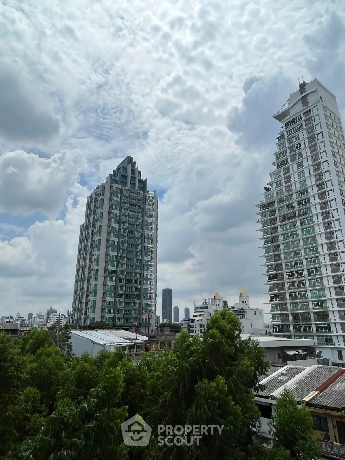 Stunning cityscape view with modern high-rise buildings and lush greenery under a dramatic cloudy sky.