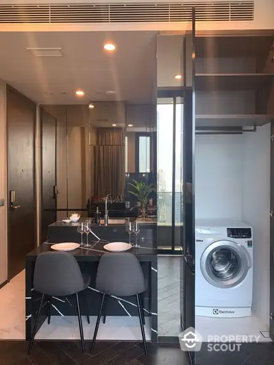 Sleek modern kitchen with integrated appliances and dining area, featuring a large window with natural light and a washing machine.