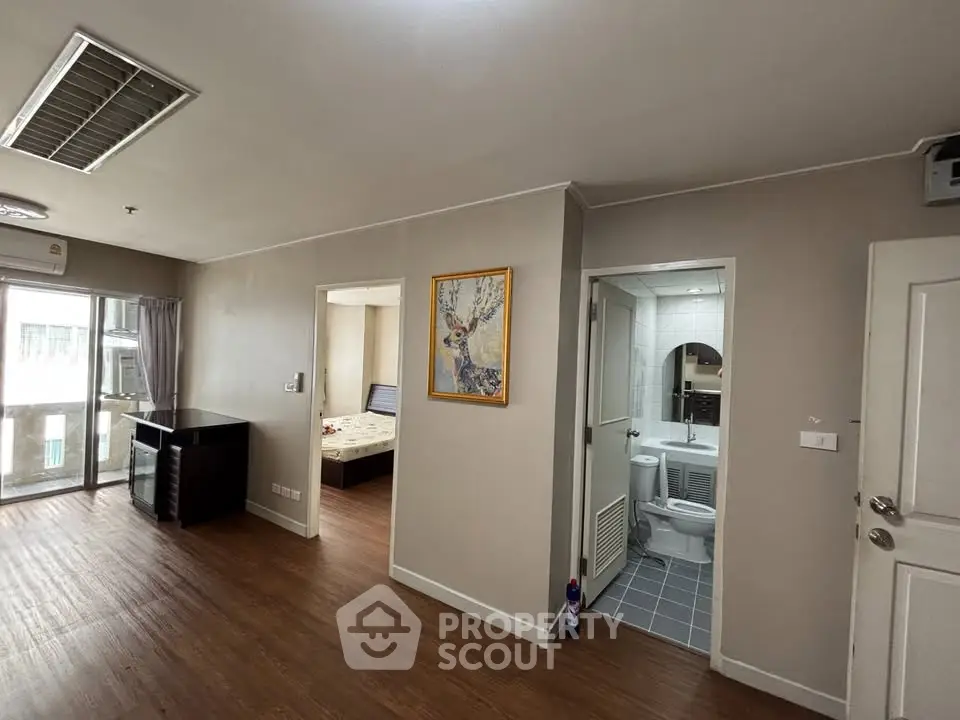 Spacious apartment interior with wooden flooring, featuring a bedroom and bathroom entrance.