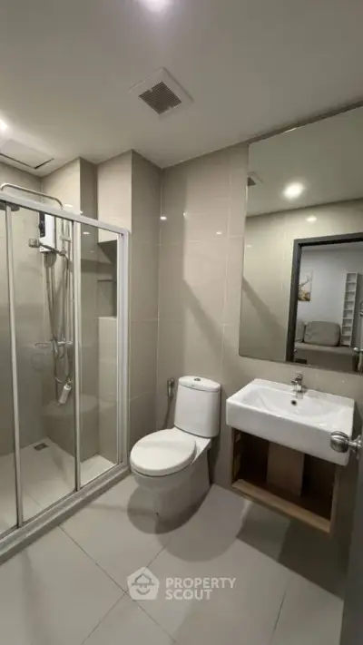 Modern bathroom with glass shower, sleek sink, and neutral tiles in a contemporary apartment.