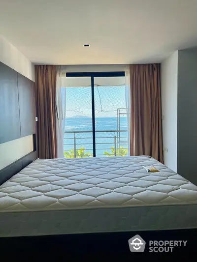 Serene bedroom with plush bedding and direct ocean view, complemented by elegant drapery and modern design, ideal for a tranquil living experience.