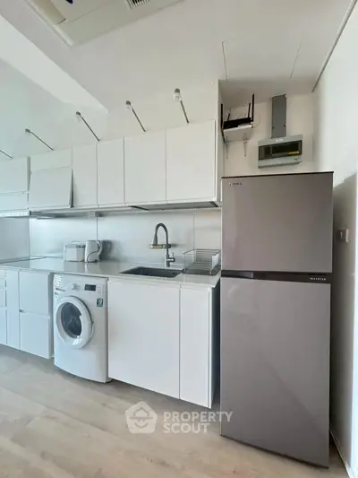 Modern kitchen with sleek cabinets, washing machine, and fridge in a compact layout.