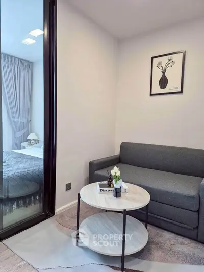 Modern living room with cozy gray sofa and stylish decor adjacent to a bedroom with elegant curtains.