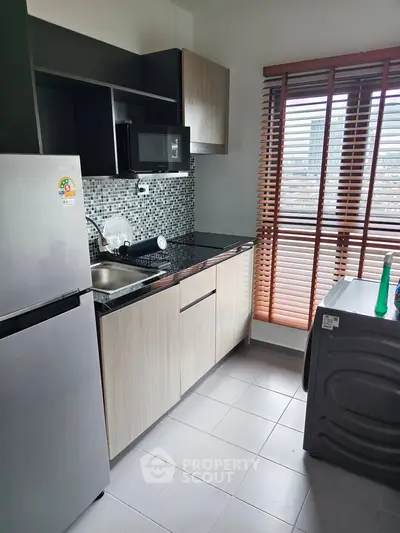 Modern kitchen with sleek appliances and city view from window blinds.