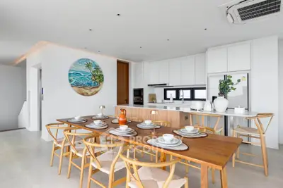 Spacious modern kitchen with dining area, featuring sleek white cabinetry and a large wooden table.