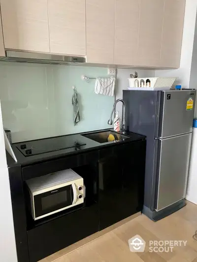 Modern compact kitchen with sleek black cabinetry and stainless steel appliances.