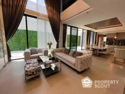 Luxurious spacious living room with elegant furniture, floor-to-ceiling windows, and modern open layout leading to a sleek kitchen.