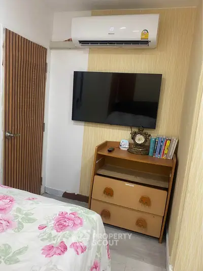 Cozy bedroom with modern air conditioning and wall-mounted TV, featuring a stylish wooden dresser.