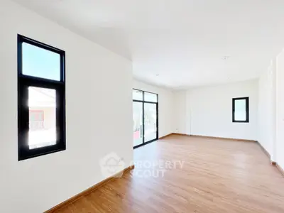 Spacious empty room with wooden flooring and large windows for natural light.
