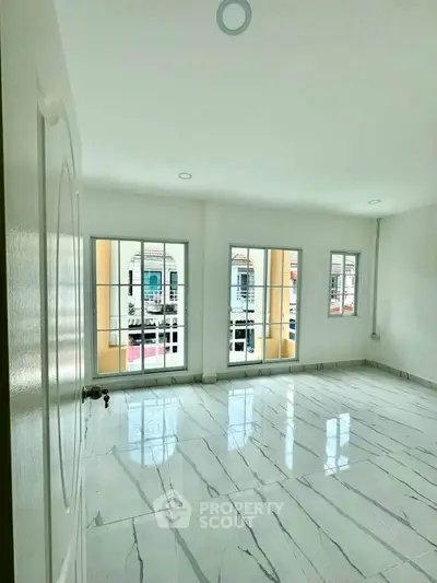 Spacious sunlit room with elegant marble flooring and large windows offering a charming view.