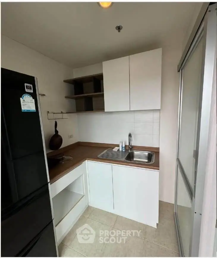 Modern compact kitchen with sleek white cabinets and black fridge in a cozy apartment.
