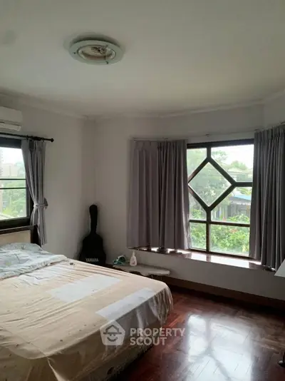 Cozy bedroom with large windows and wooden flooring, offering serene garden views.