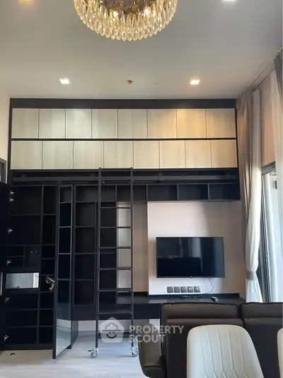 Modern living room with built-in shelving, TV, and elegant chandelier