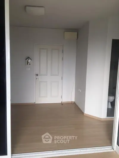 Spacious entryway with wooden flooring and modern white door in a minimalist apartment.