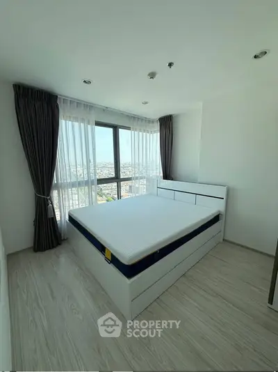 Bright bedroom with large window and city view, featuring modern furniture and elegant curtains.