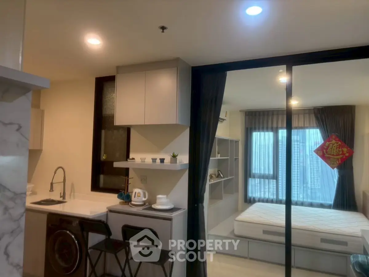 Modern studio apartment with open kitchen and cozy living space, featuring large windows and stylish decor.
