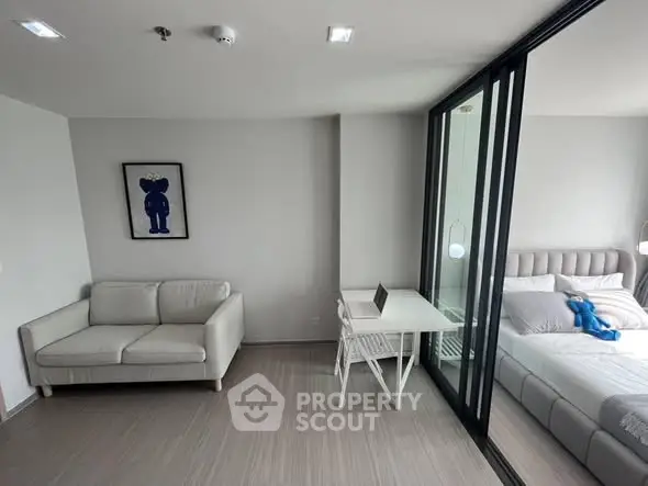 Modern apartment interior with cozy living area and stylish bedroom separated by glass partition.