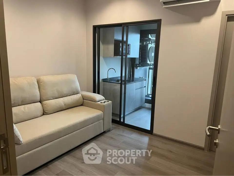 Cozy living room with modern sofa and view into sleek kitchen with glass sliding doors.