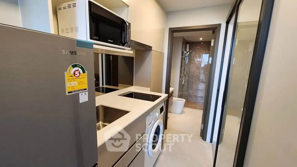 Modern compact kitchen with appliances and adjacent bathroom in sleek apartment.