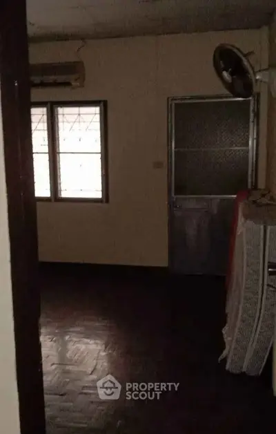 Dimly lit room with window and door, featuring a fan and air conditioner.
