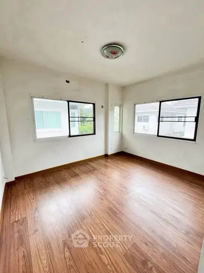 Spacious empty room with wooden flooring and large windows offering natural light.