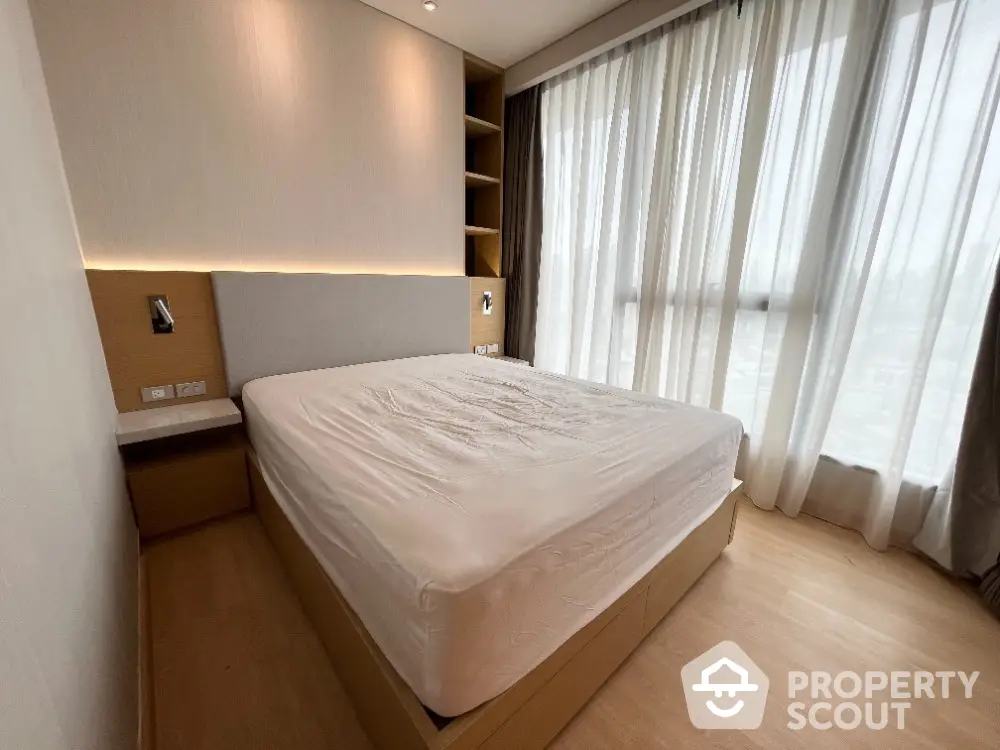 Modern bedroom with large window and built-in shelves, featuring a minimalist design and natural light.