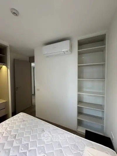 Modern bedroom with built-in shelves and air conditioning unit, featuring a comfortable mattress.