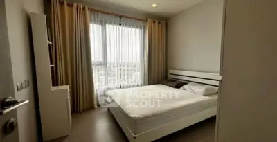 Spacious bedroom with large window and modern furnishings in a high-rise apartment.