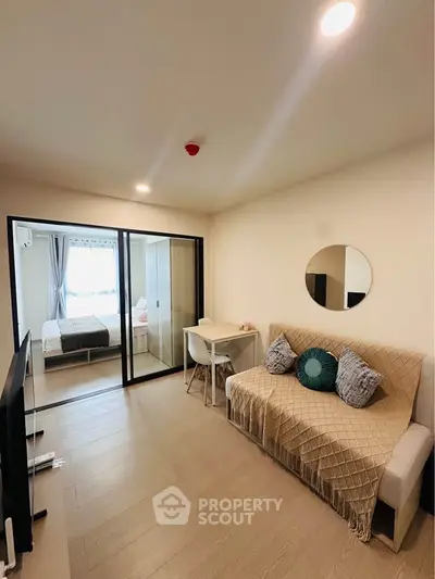 Modern living room with cozy sofa and stylish decor leading to a chic bedroom through sliding glass doors.