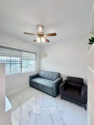 Modern living room with sleek furniture and ceiling fan, featuring large window and glossy tile flooring.