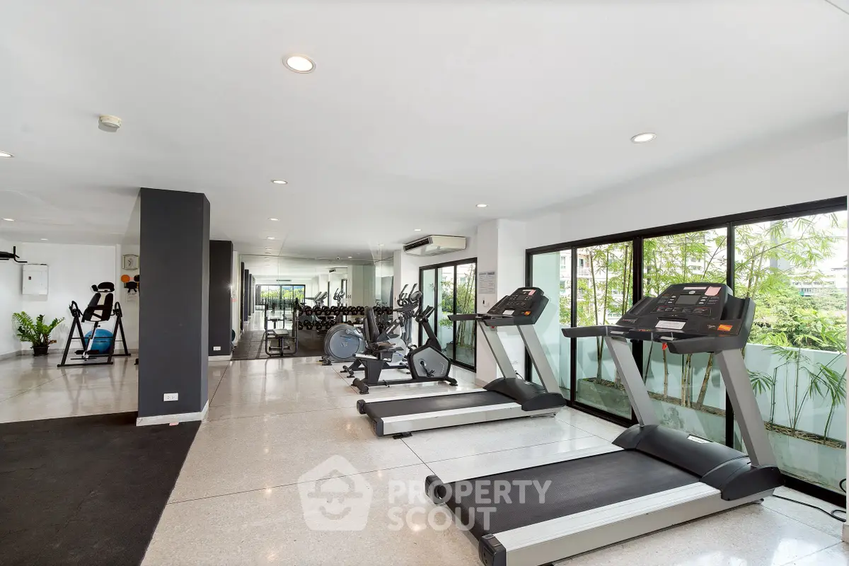 Spacious modern gym with state-of-the-art equipment and large windows offering lush greenery views.